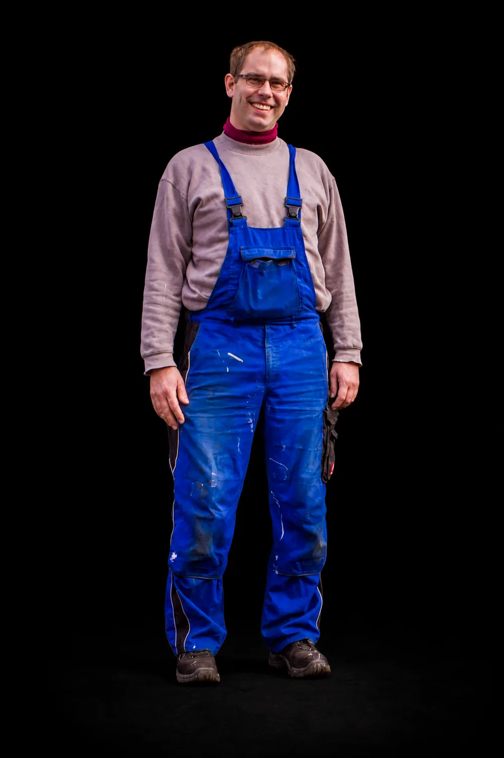 Harald Bayer im blauen Werkstattanzug vor schwarzem Hintergrund